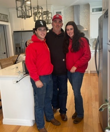 Man with two young adults in a kitchen; all wearing red hoodies and jeans.
