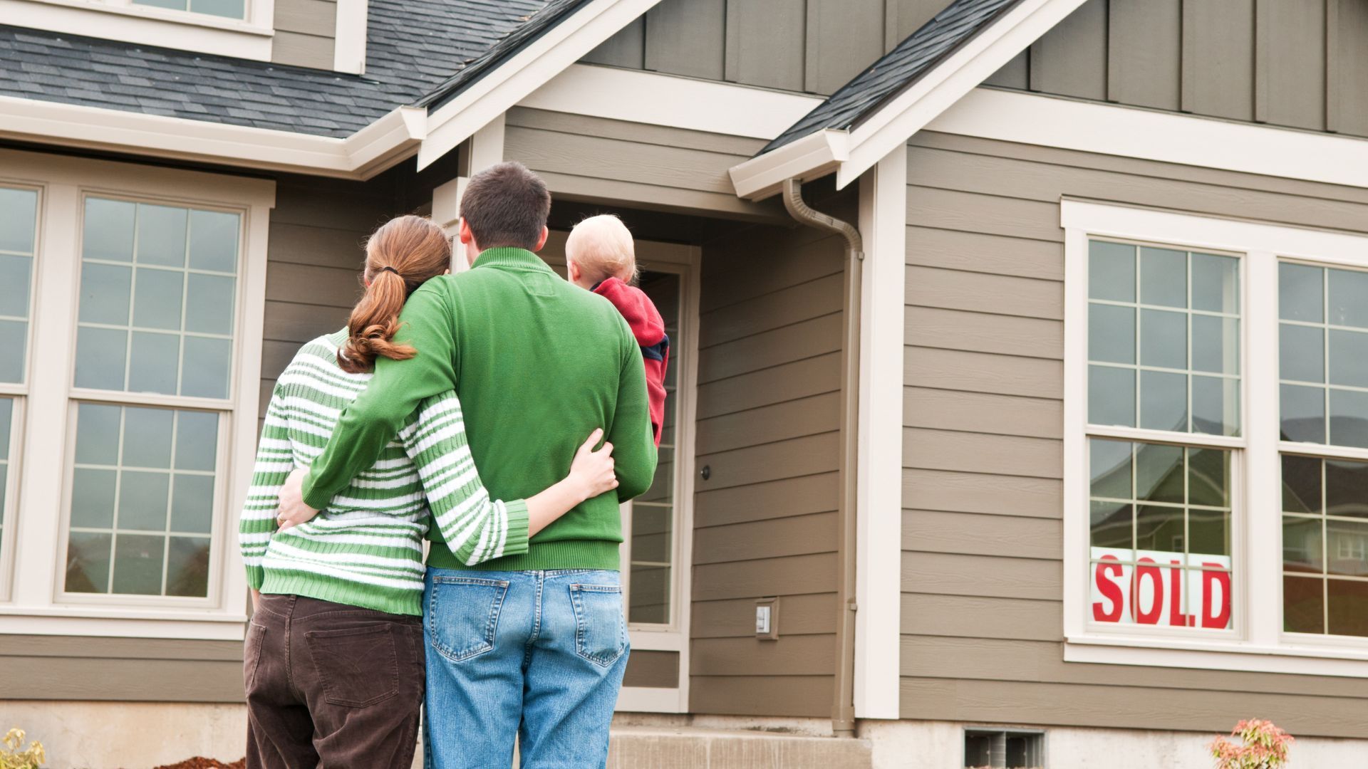 A family is standing in front of a house that has been sold.