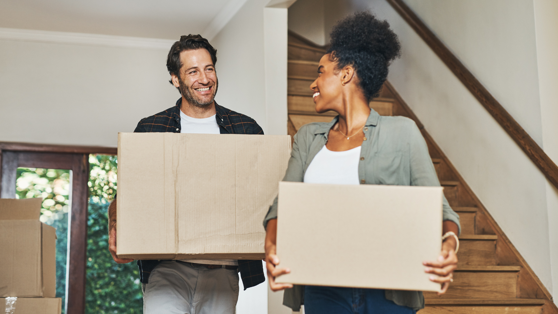 A man and a woman are holding cardboard boxes in their new home.