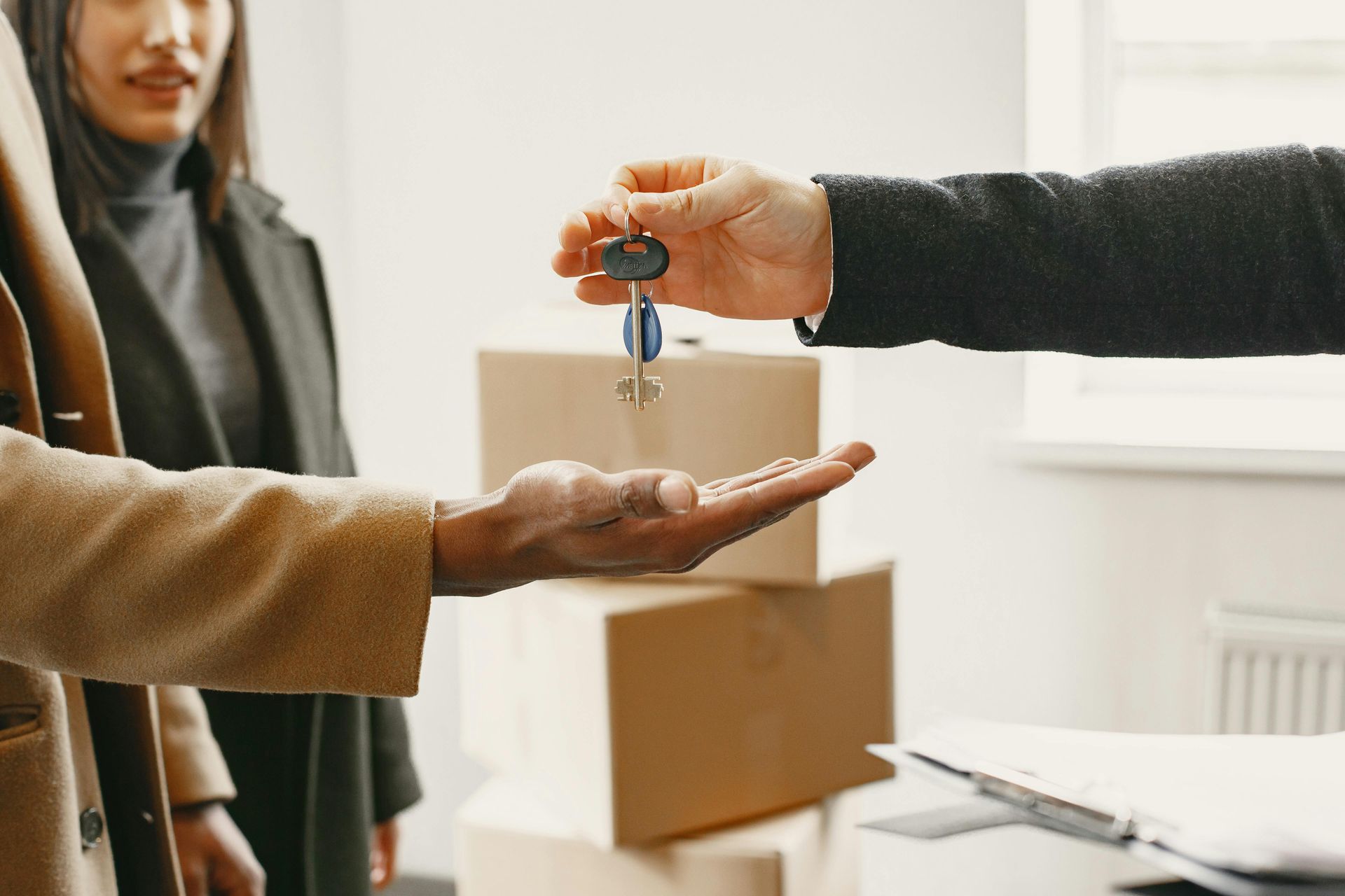 A person hands a set of keys to another individual in an room filled with moving boxes.