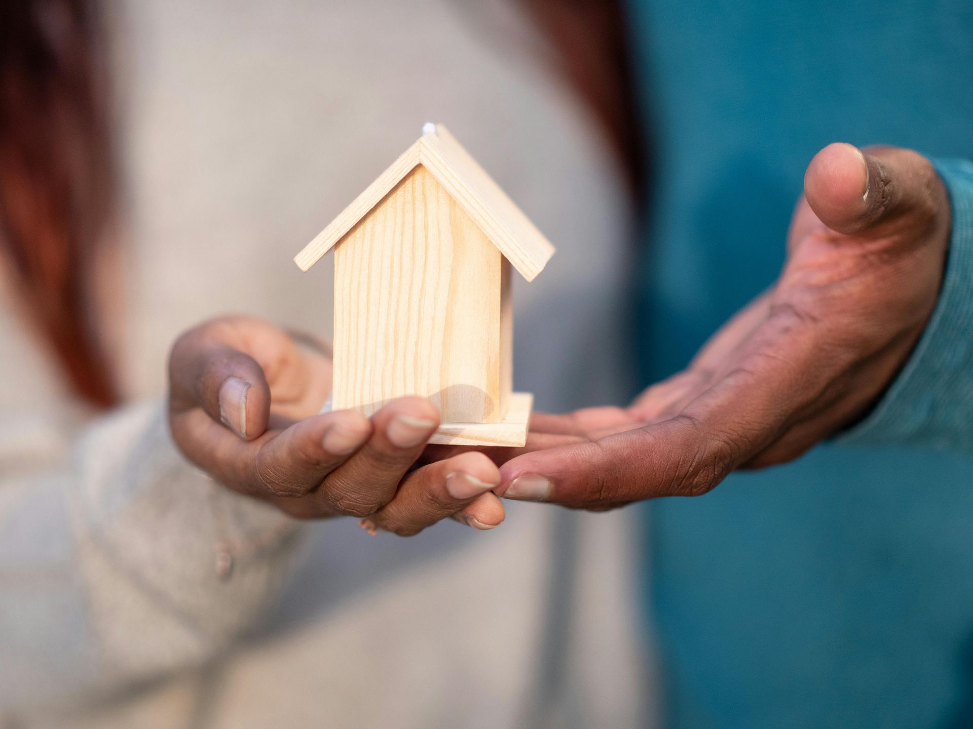 Hands holding a small wooden house.