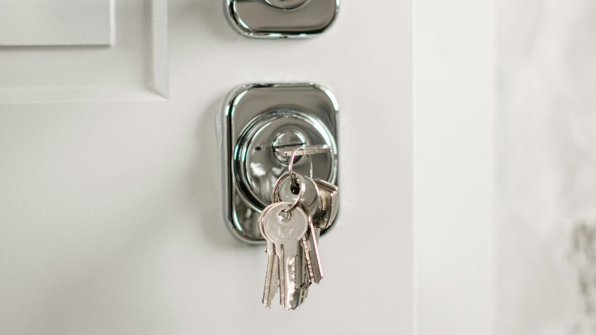 House key inserted in a silver door lock on a white door