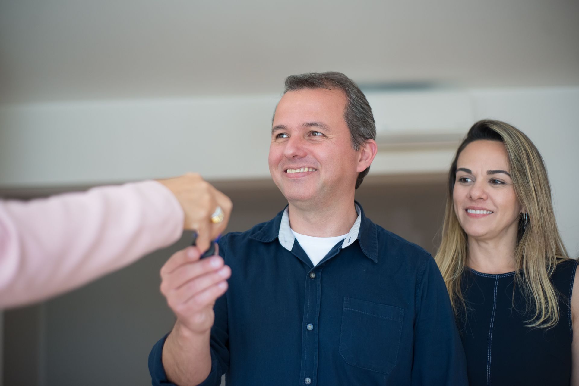 Two smiling people receiving a key from an outstretched hand indoors