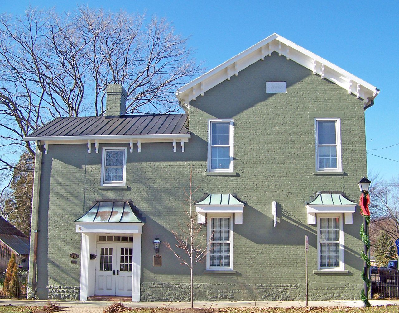 Green brick two-story building with white trim, windows, and awnings; blue sky.
