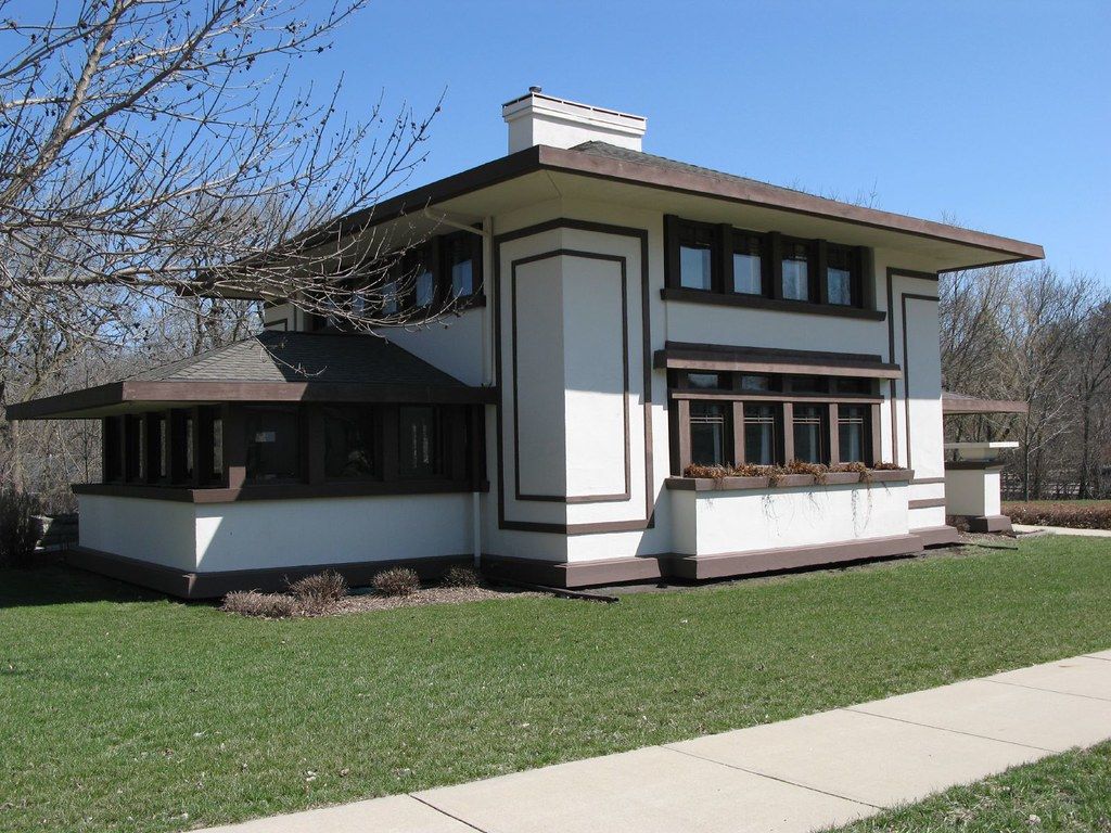 A white house with brown trim sits on a lush green lawn