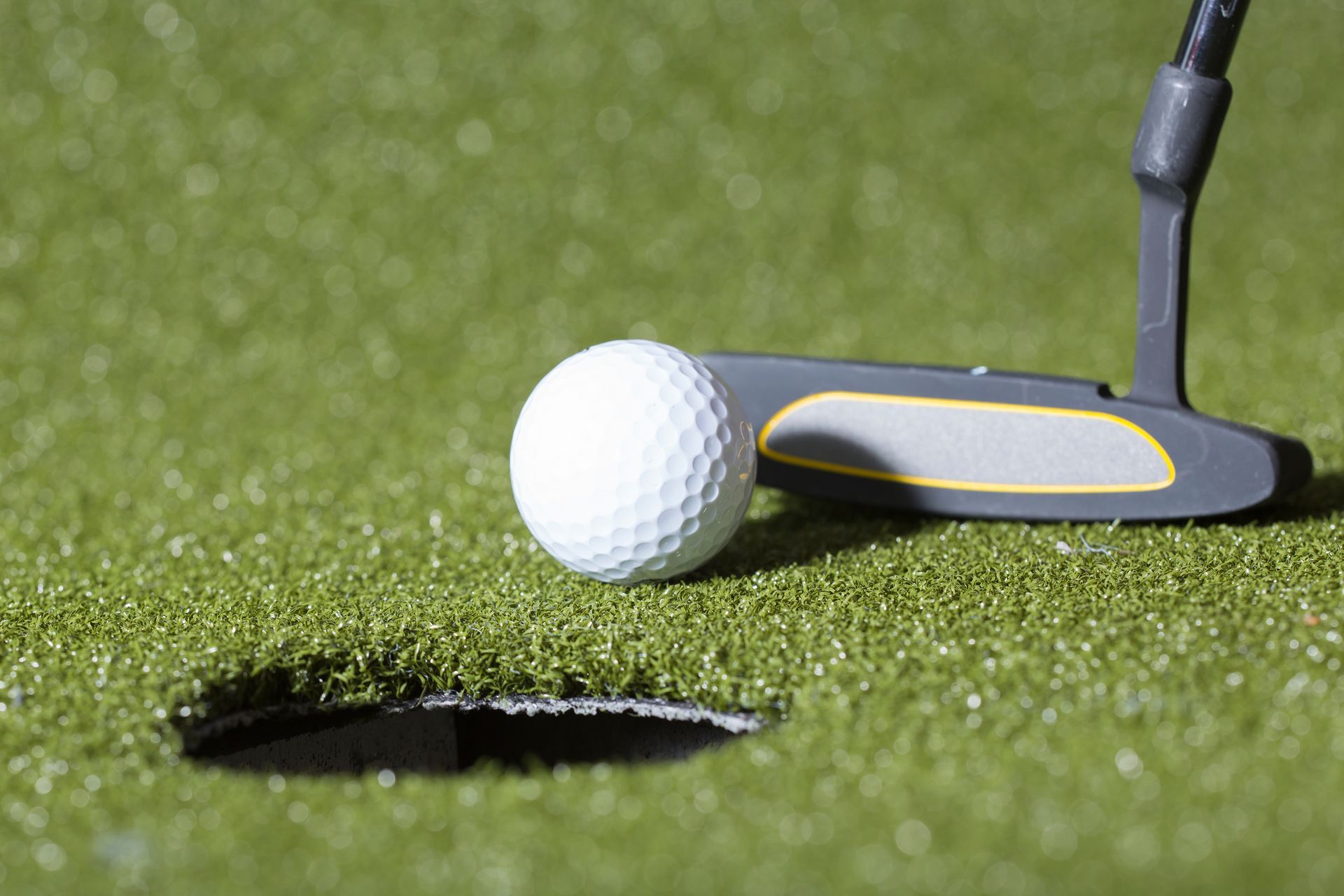 Golf ball near the hole, about to be putted. Putter and green grass are in view.