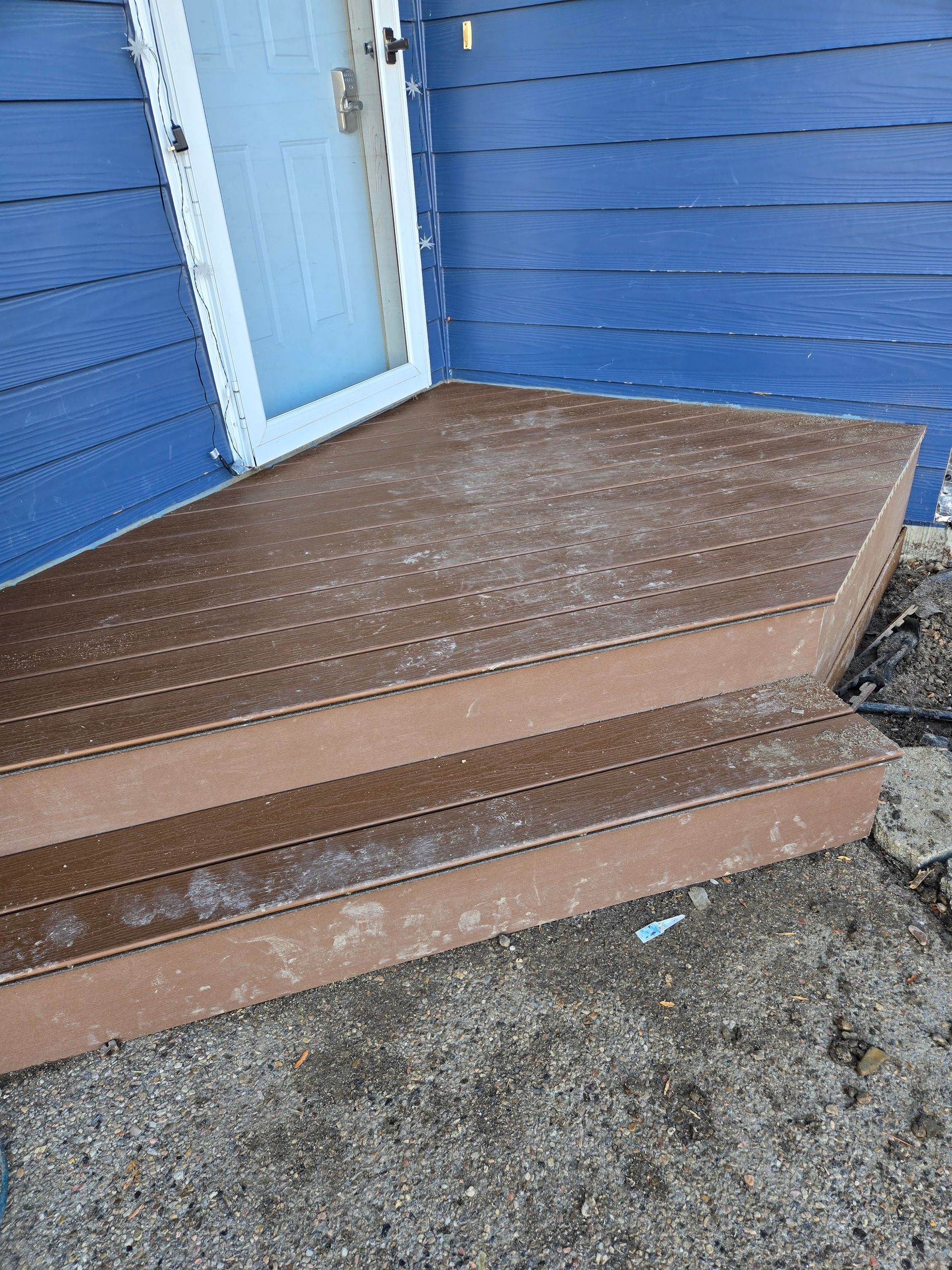 A two-step brown deck platform with a light blue door on a house with blue siding.