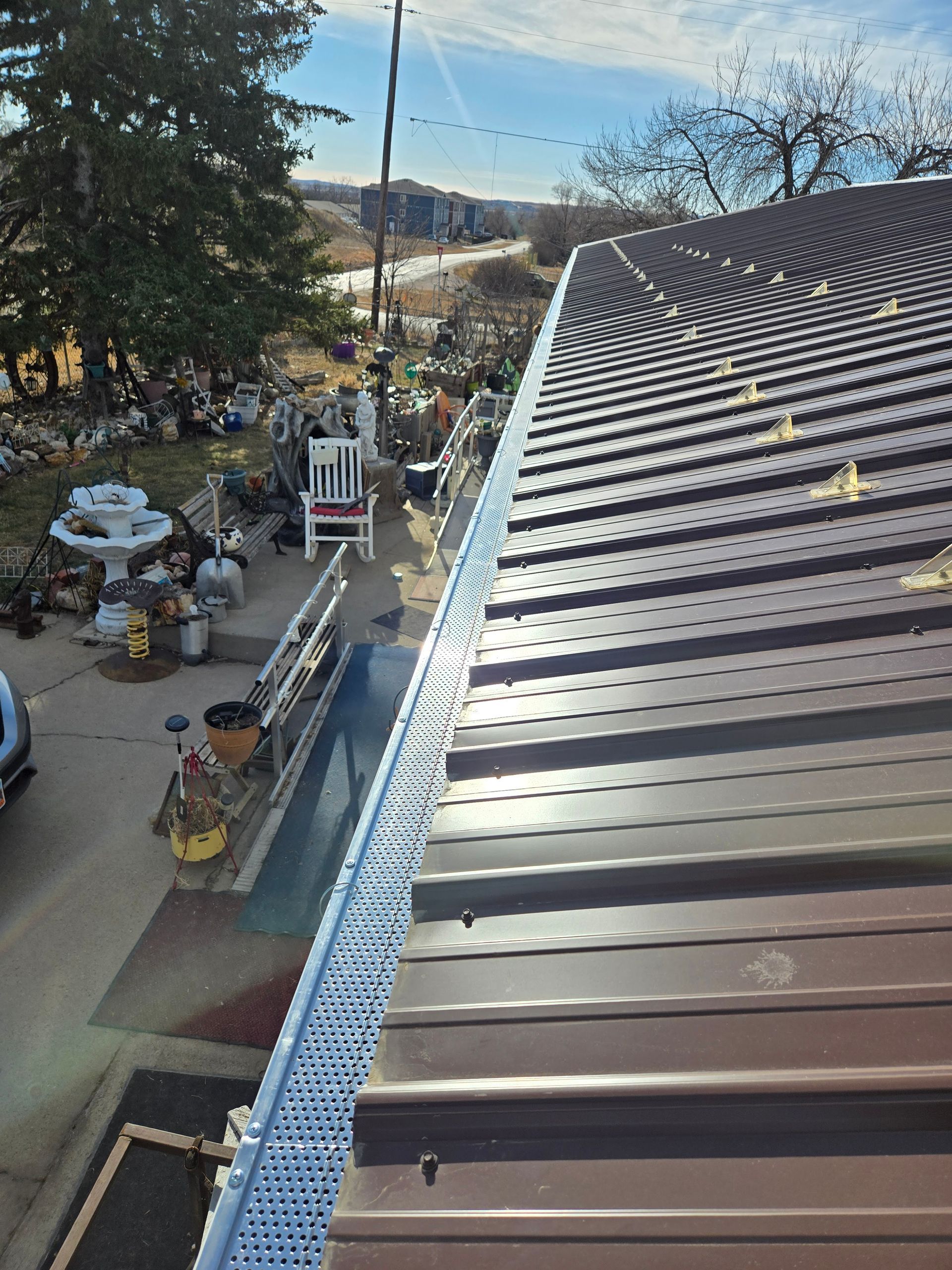 An elevated view of a brown metal roof featuring a perforated metal gutter guard along the eaves.