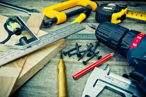 A variety of carpenter's tools, including a drill, clamp, ruler, pencil, and screws, scattered on a wooden workbench.