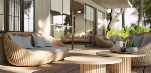 Wicker outdoor sofas and matching round tables on a sunlit wooden patio in front of a modern house.