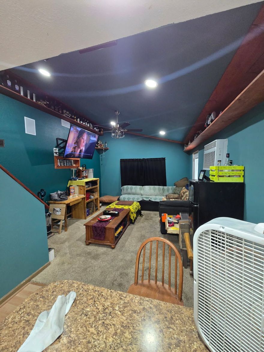 A living room with teal walls, a dark ceiling, a mounted television, a wooden coffee table, and a sofa in the background.