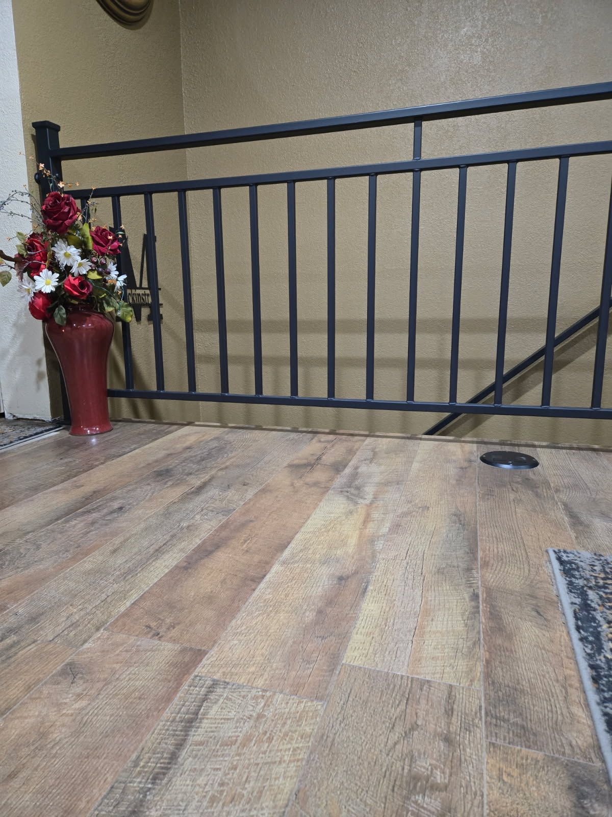 A wood-look floor leads to a black metal railing with a red vase of flowers next to it.