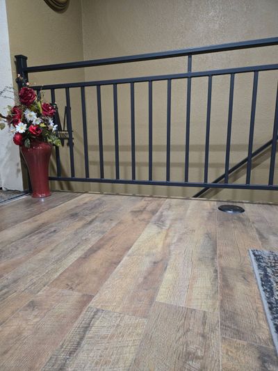 A wood-look floor leads to a black metal railing with a red vase of flowers next to it.