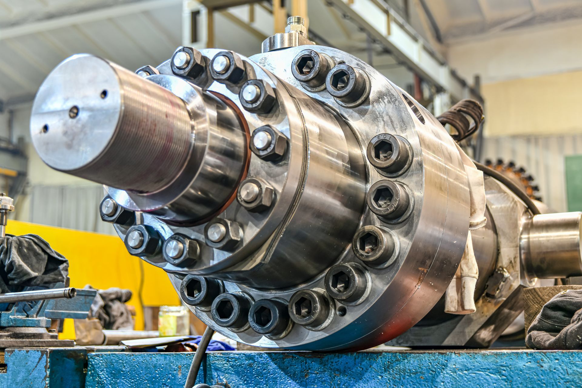 A heavy-duty hydraulic cylinder with a bolted flange assembly, resting on a workbench in a machine shop.