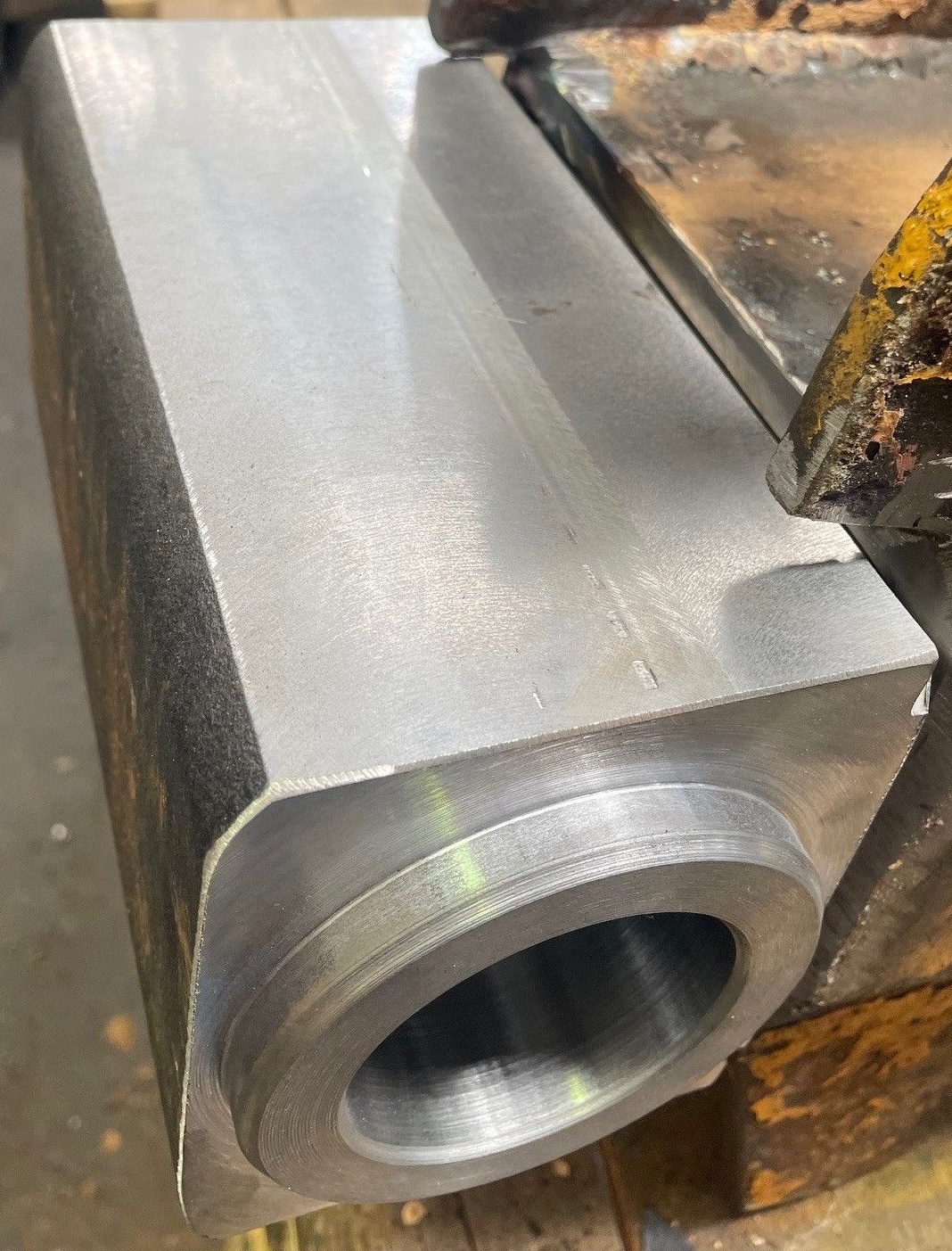 Metal block being machined in a lathe, with a smooth silver surface and cutting tool nearby.