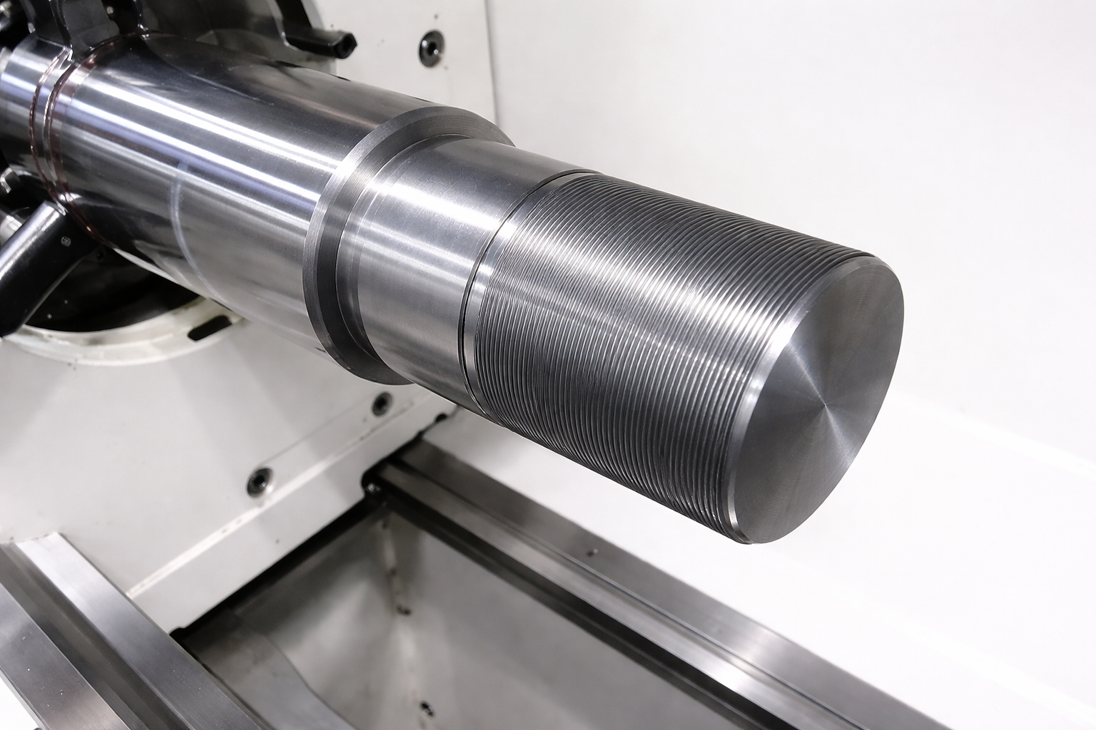 Close-up of a polished metal shaft on a lathe, with a textured cylindrical end piece. Close-up of a polished metal shaft on a lathe, with a textured cylindrical end piece.