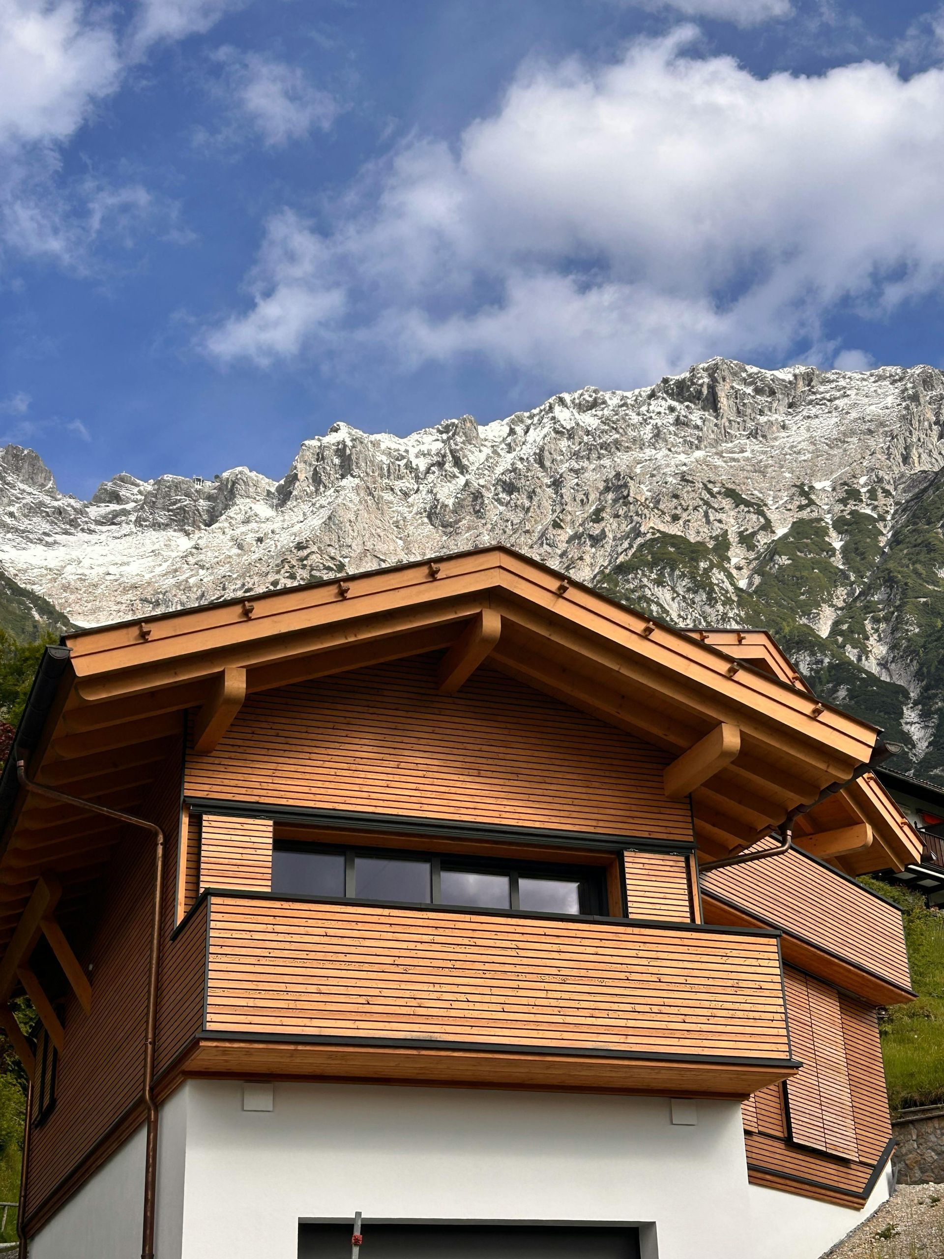 Wooden chalet with tiled roof in front of snowy mountain peaks under a blue sky