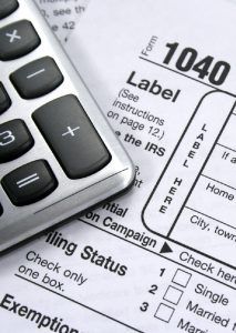Calculator on top of a 1040 tax form with filing status and exemption sections visible.