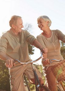 Smiling couple riding bicycles outdoors. Sunny, light-colored clothing.