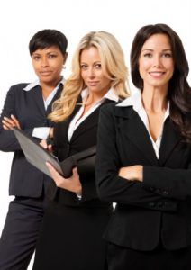 Three women in business suits, standing together with arms crossed; professional setting.