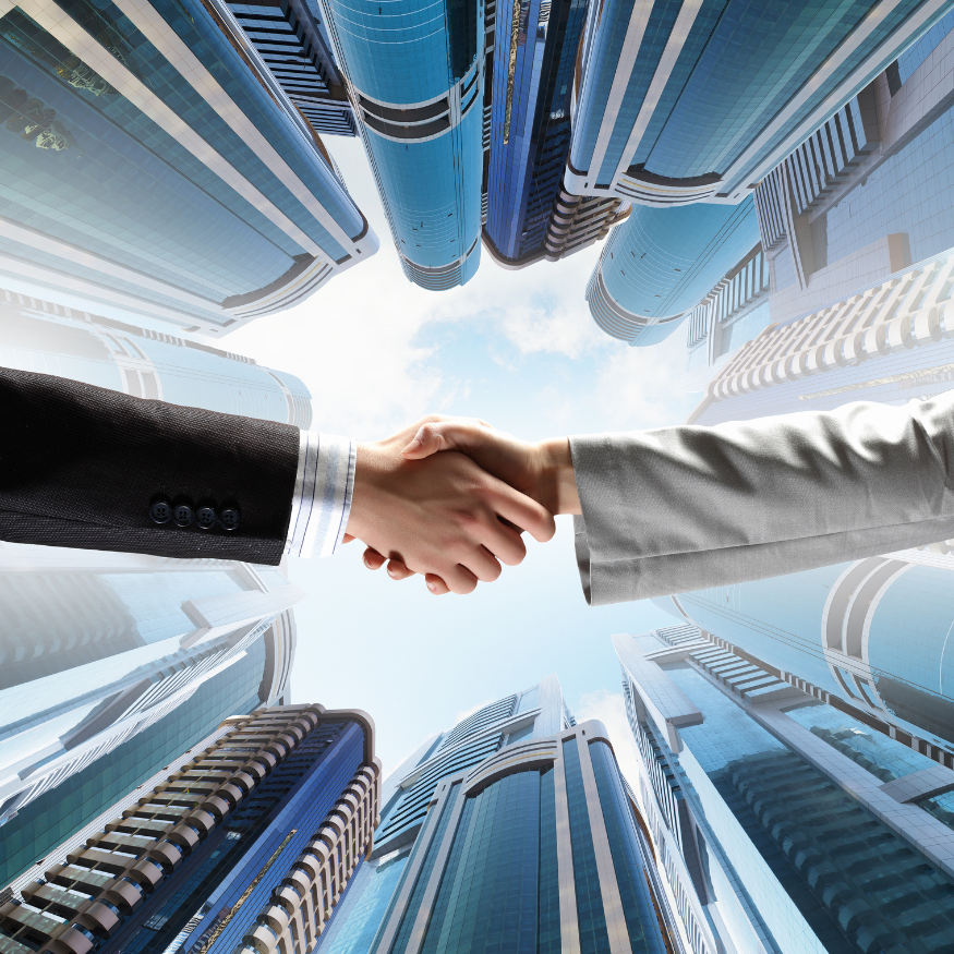 Two people shaking hands, viewed from below with tall skyscrapers.