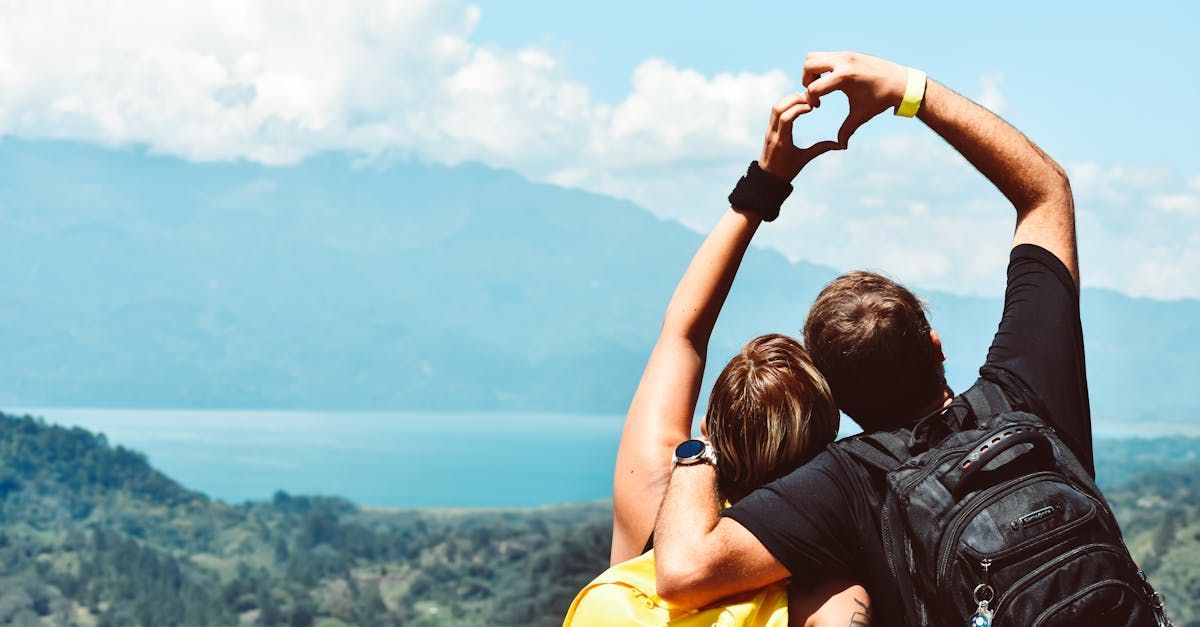 Couple making heart with hands overlooking mountains and lake.