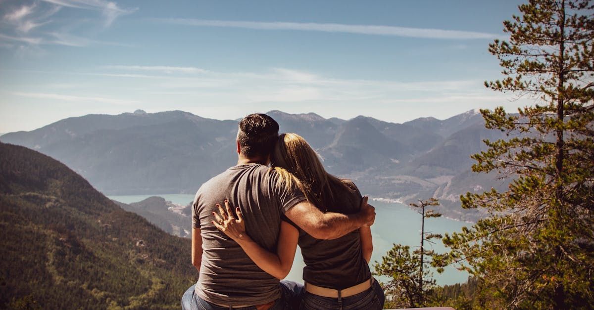Couple with arms around each other overlooking a mountain lake on a sunny day.
