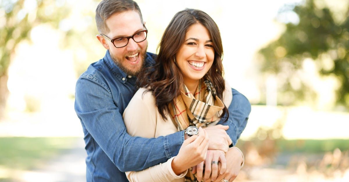 Man hugging woman from behind, both smiling outdoors.