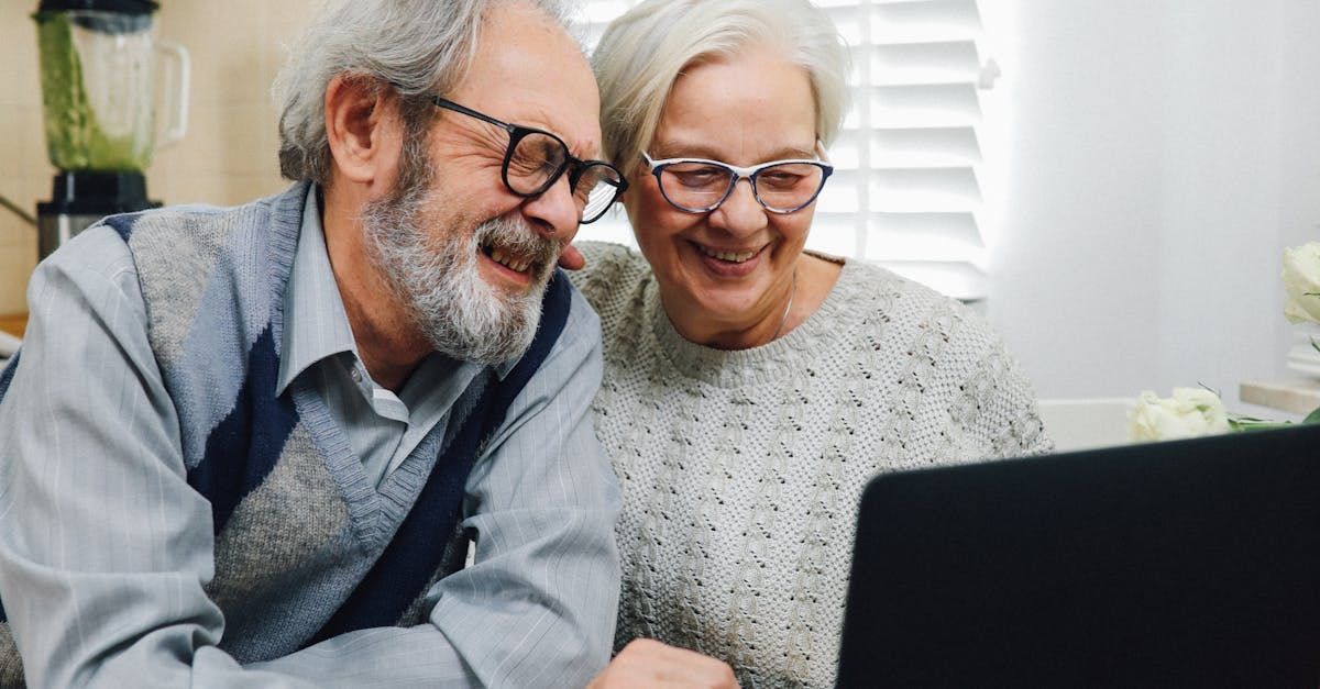 Elderly couple smiling at a laptop screen in a kitchen, looking happy.