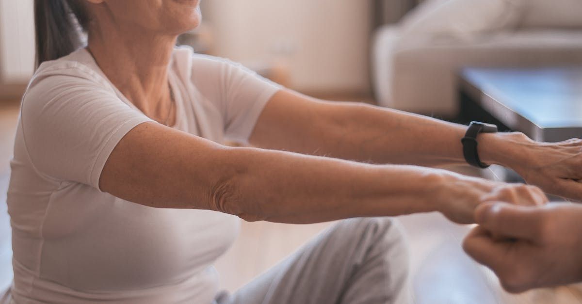 Person holding hands, performing a stretching exercise indoors, wearing a white t-shirt.