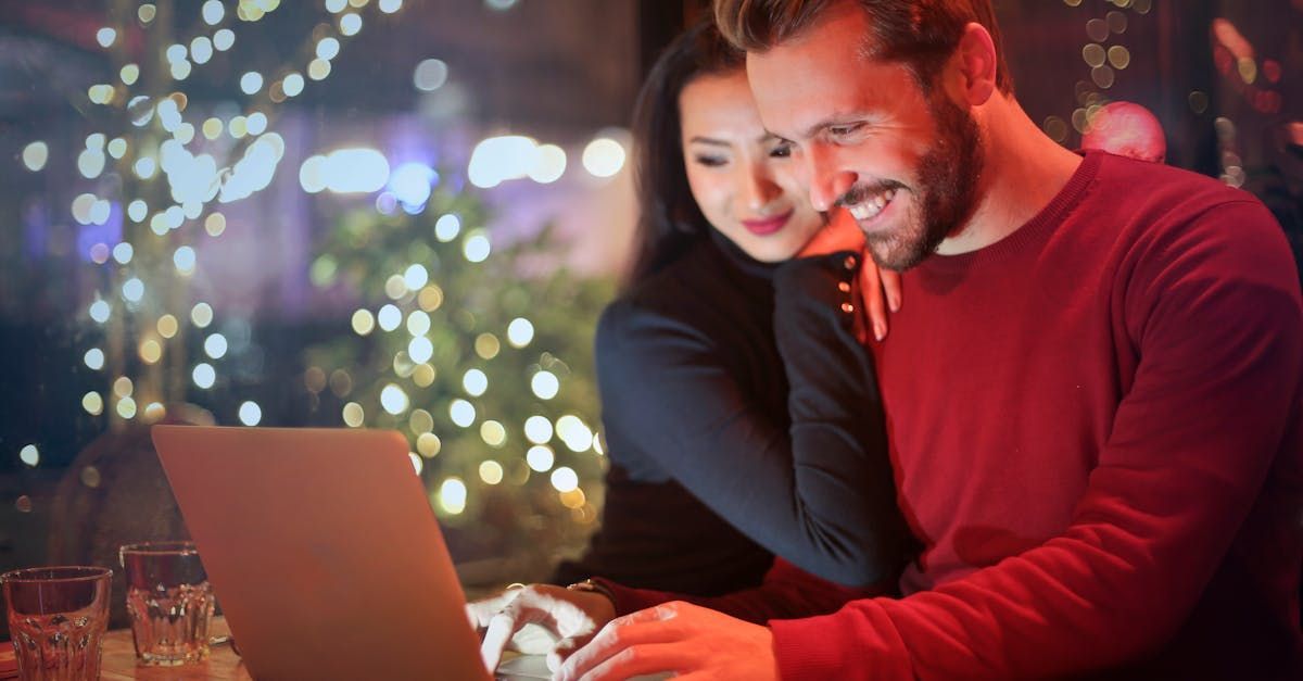 Couple looking at a laptop with smiles, outdoors at night with string lights.