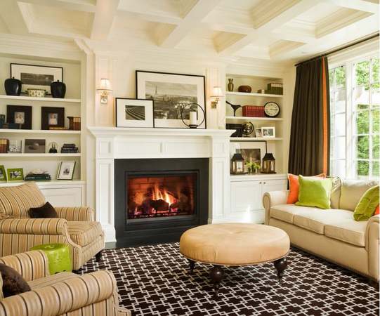 Cozy living room with fireplace, built-in shelves, patterned rug, sofa, chairs, ottoman, and large window.
