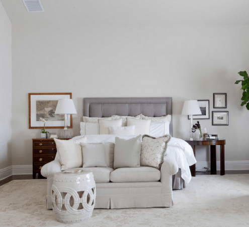 A light-filled bedroom with a bed, small sofa, and two nightstands. Soft neutral tones.
