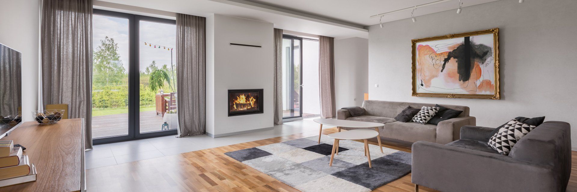 Living room with fireplace, sofas, and large windows with a view of the outdoors.