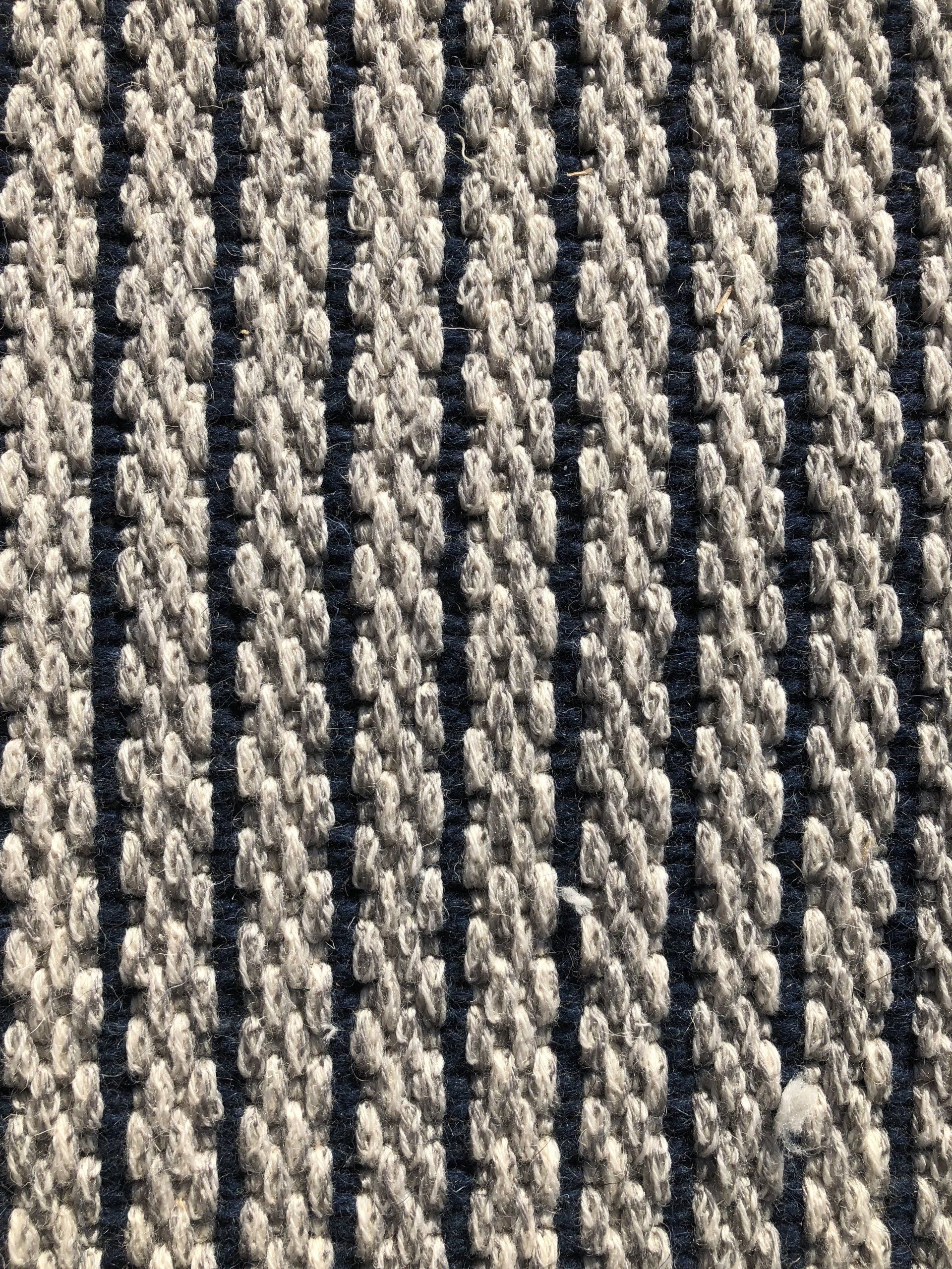 Close-up of a woven rug with vertical stripes in off-white and dark blue.