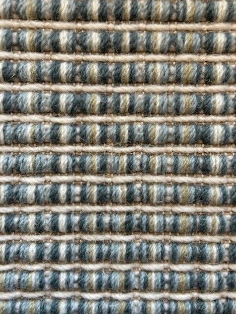 Close-up of a woven rug with horizontal stripes in blue-gray, olive, and cream.