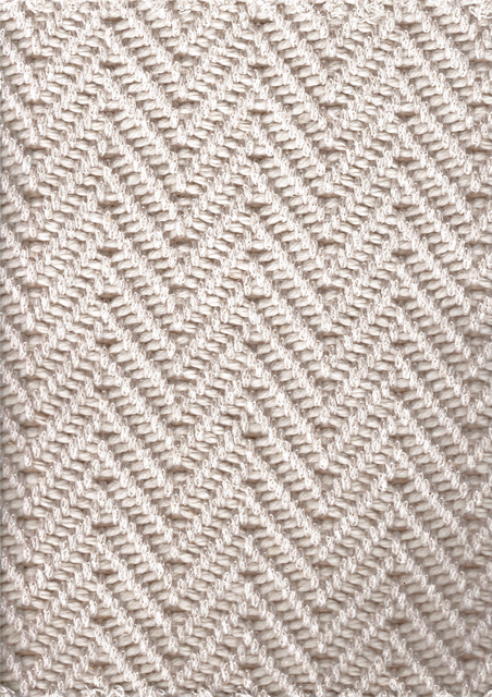 Close-up of a woven rug in a repeating, diagonal herringbone pattern. Beige color with texture.