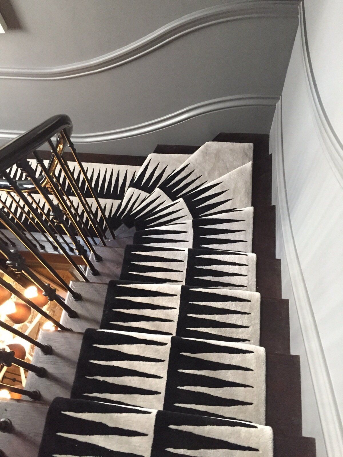 Staircase with black and white patterned runner. Dark wood stairs, ornate railing, light grey walls.