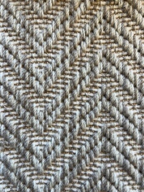 Close-up of a woven fabric with a repeating diamond pattern in shades of gray and beige.
