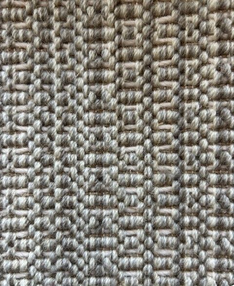 Close-up of a woven rug with a textured, geometric pattern in shades of gray.