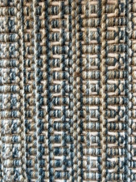 Close-up of a woven rug with vertical stripes of alternating blue and tan yarns.