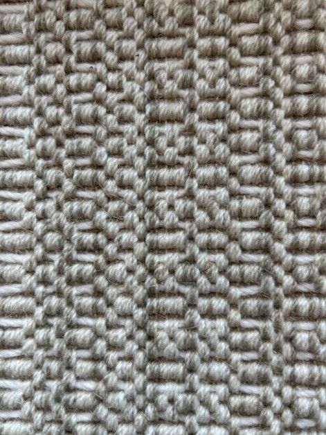 Close-up of a textured, light beige woven fabric with a geometric pattern.