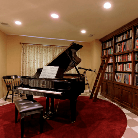 Black grand piano on red rug in a room with a bookshelf and a small ladder.