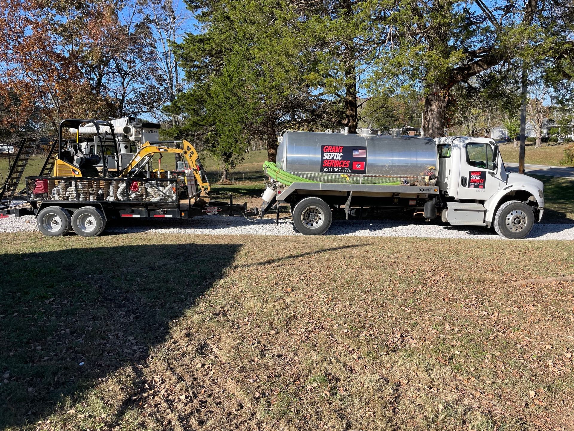 A large tanker truck is parked next to a small excavator.