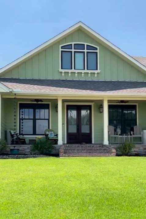 A green house with a porch and a large lawn in front of it.