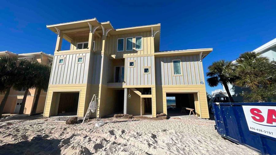 A large house is being built on the beach next to a dumpster.