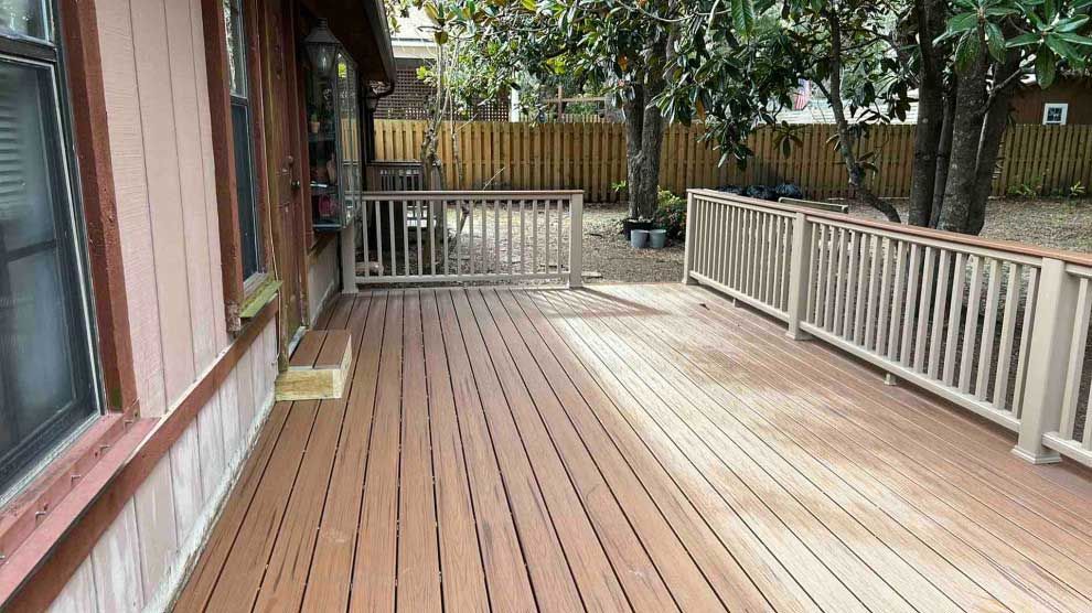 A large wooden deck with a railing in front of a house.