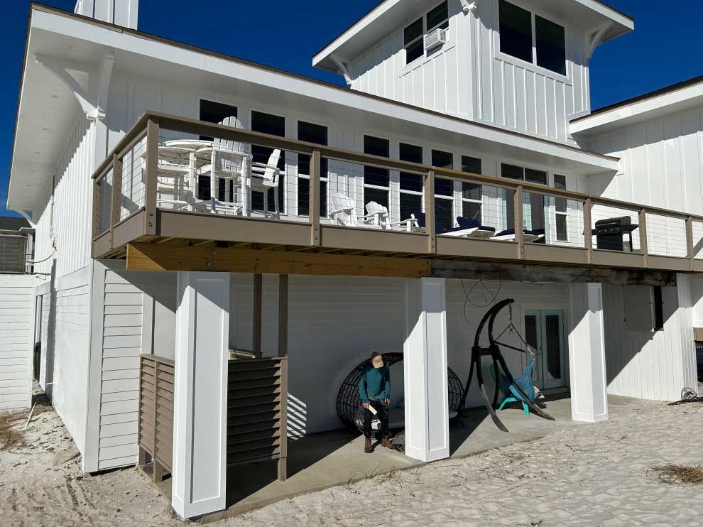 A white house with a large deck and a woman sitting on the porch.