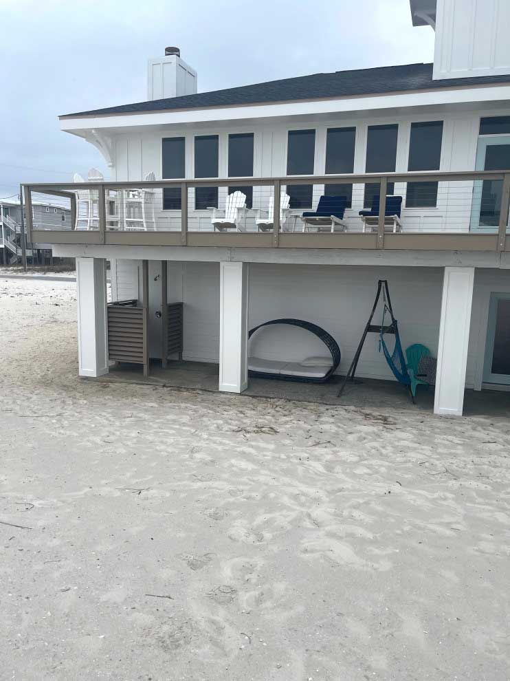 A white house with a large deck on the beach.