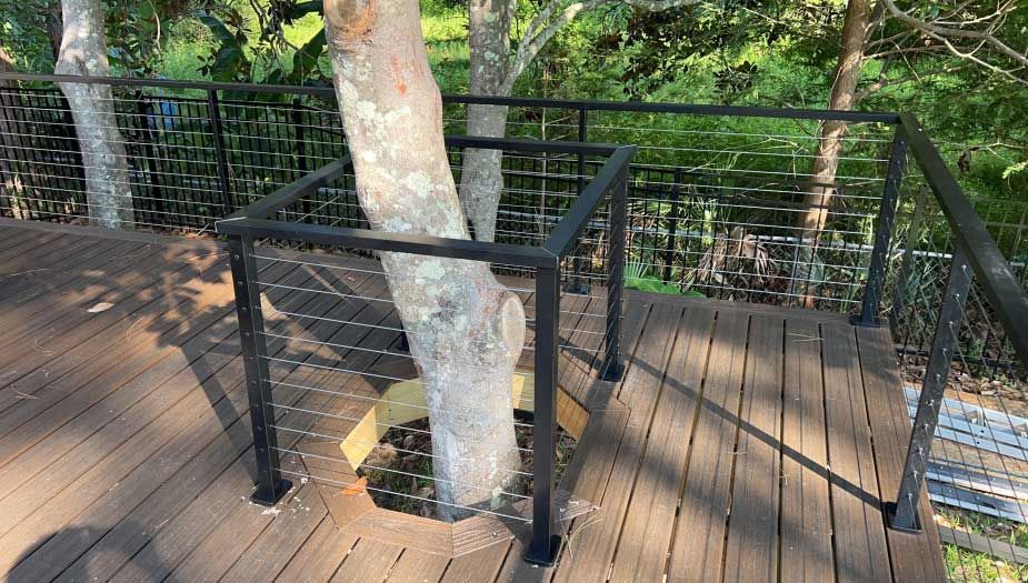 A wooden deck with a metal railing and a tree in the background.